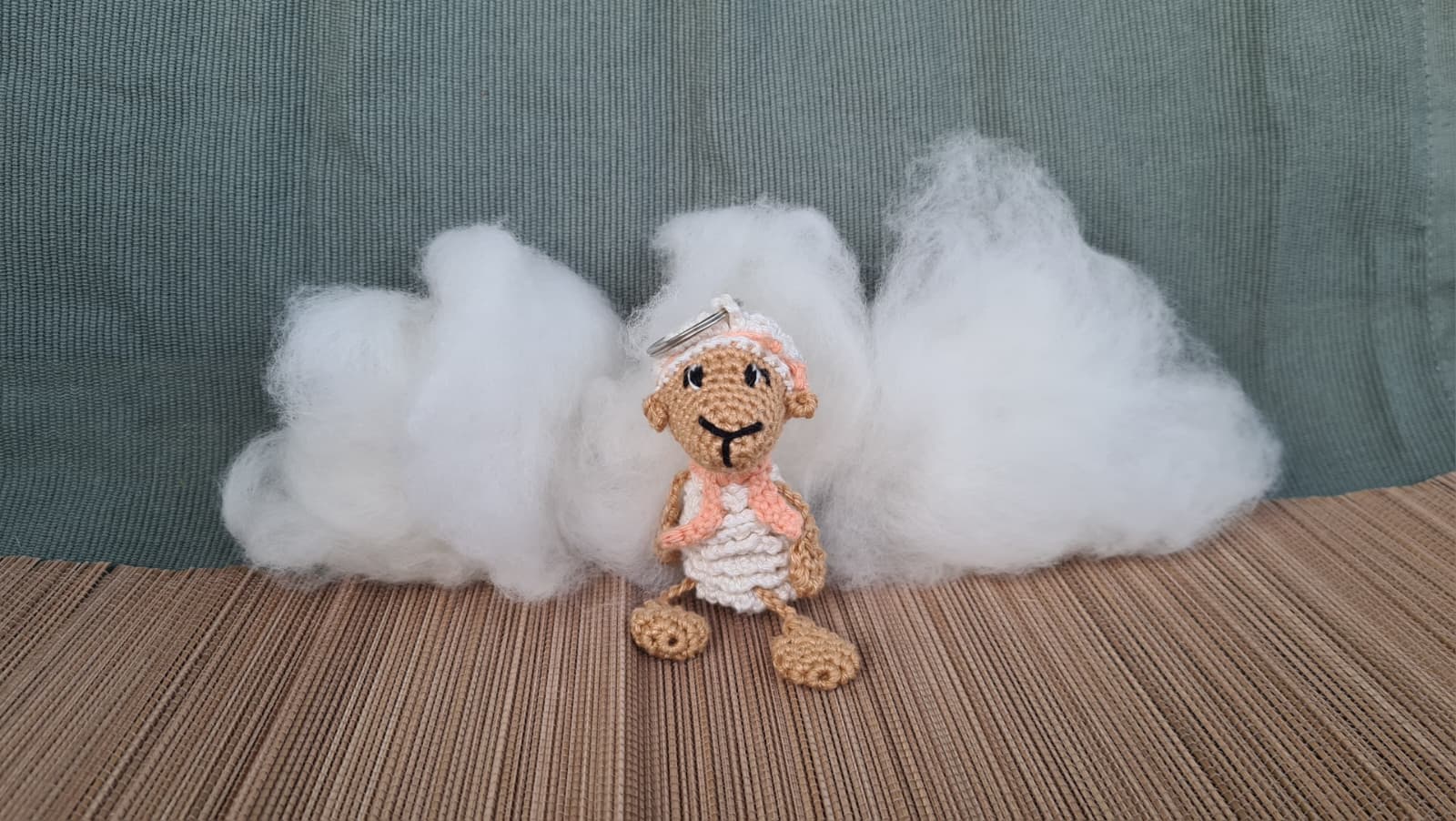 Gehäkeltes Schaf als Schlüsselanhänger vor Watte, die Wolken darstellet